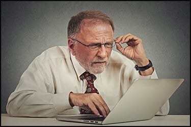 אדם מבוגר עם משקפיים יושב מבולבל מול מחשב נייד