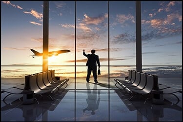איש עסקים בשדה התעופה מסתכל מחוץ לחלון גדול ורואה מטוס ממריא בשקיעה