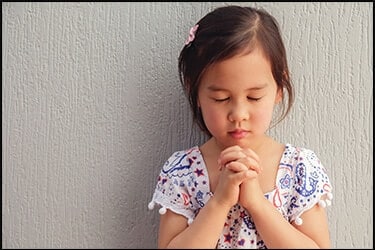 ילדה קטנה אסייתית שמתפללת בעיניים עצומות